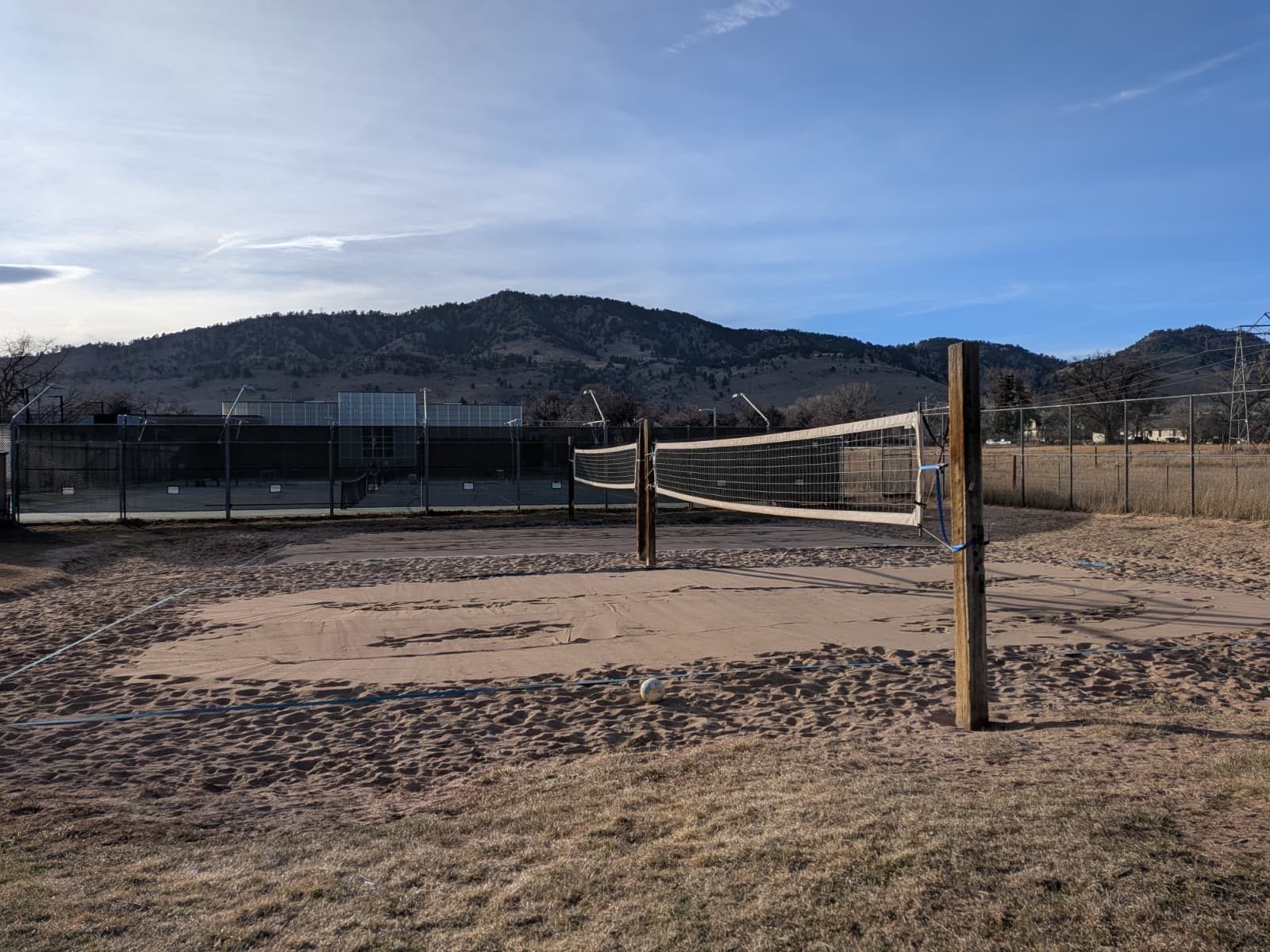 A sand volleyball court at golden hour, blue tape marking the lines, the Boulder foothills behind it.